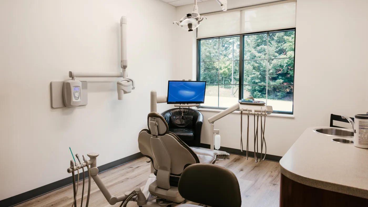 A treatment room with a wall-mounted x-ray arm beside the dental chair